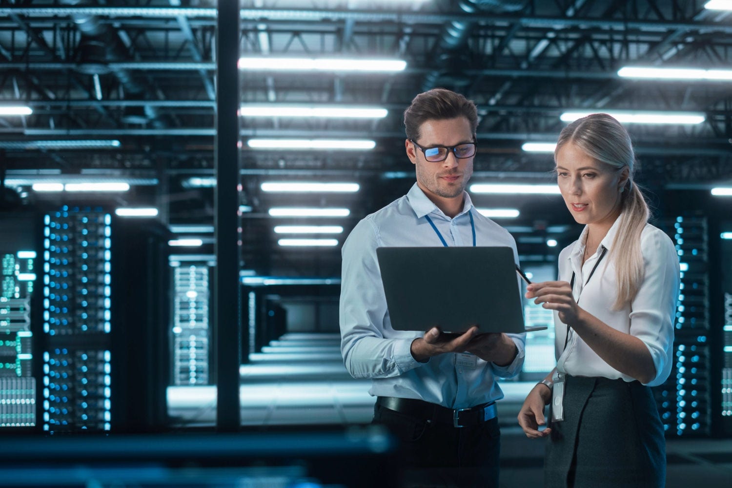 Two professionals reviewing data on a laptop in a modern data center.