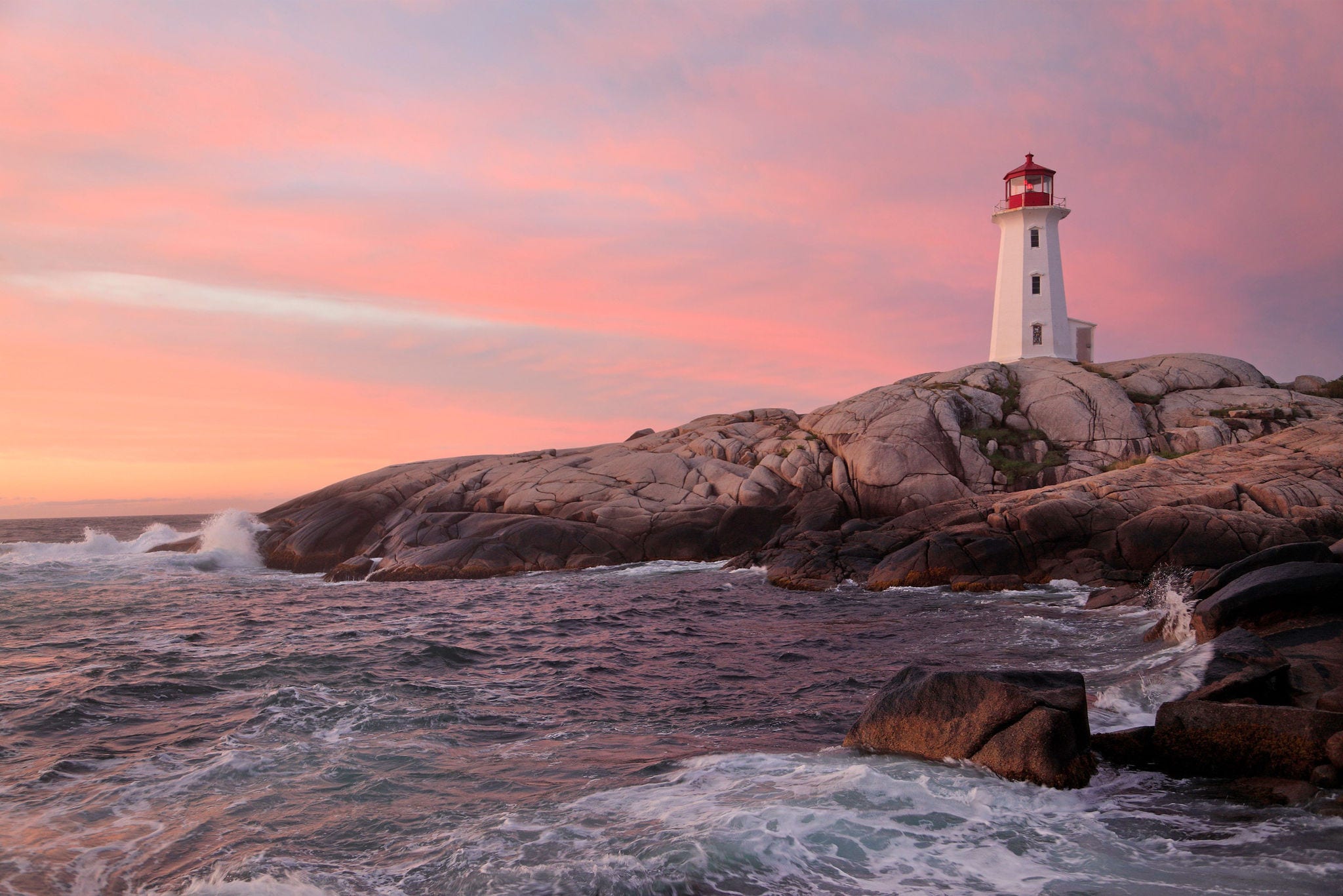 Peggy’s Cove Lighthouse illuminated at sunset with dramatic waves on the foreground, Nova Scotia, Canada