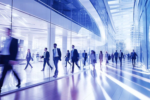 Foto com exposição longa de uma multidão de executivos caminhando rapidamente pelo saguão iluminado de um escritório, com efeito desfocado