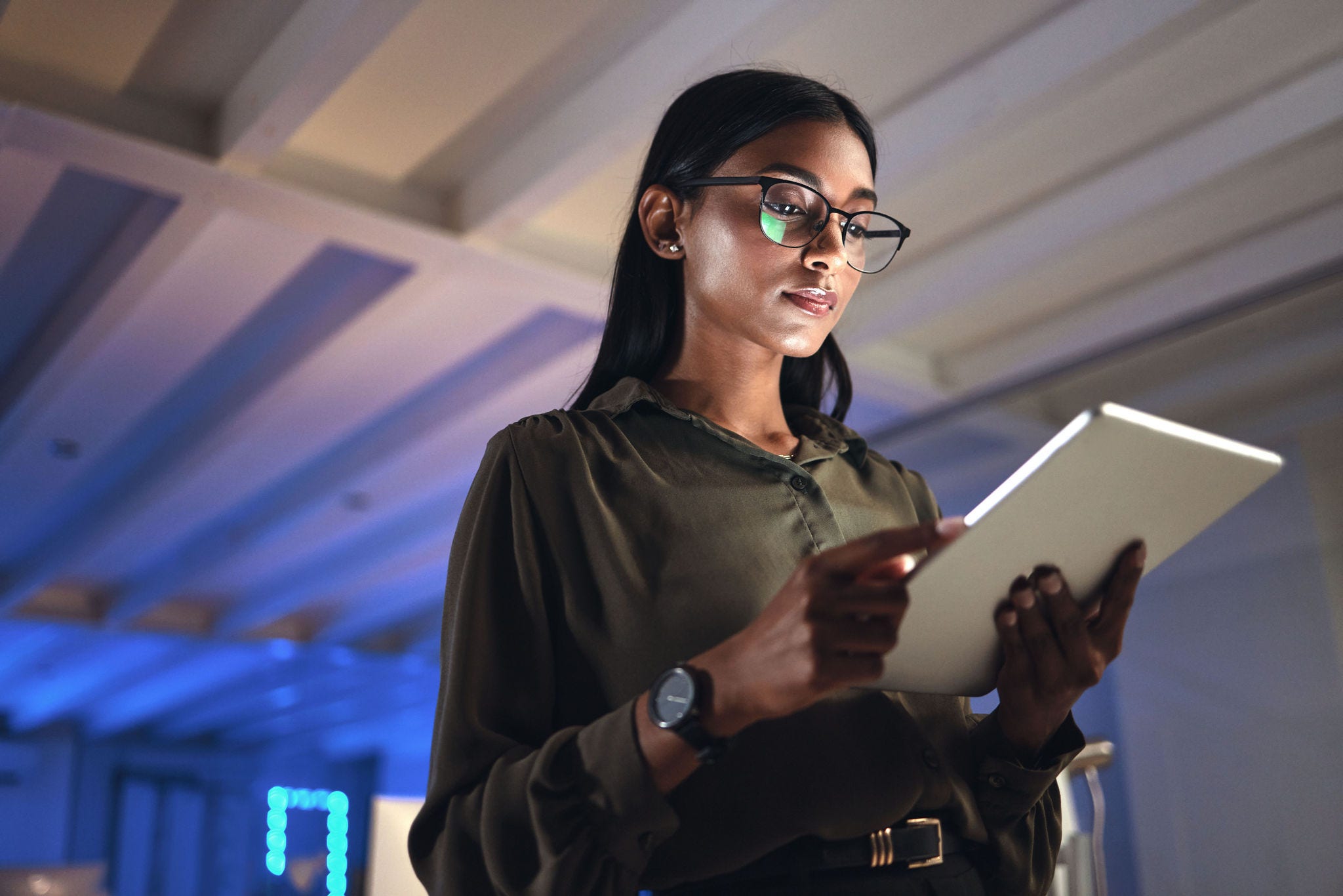 Tablet, designer and serious woman research in business startup office at night on deadline. Technology, creative professional or Indian entrepreneur reading information, email or app in neon company.