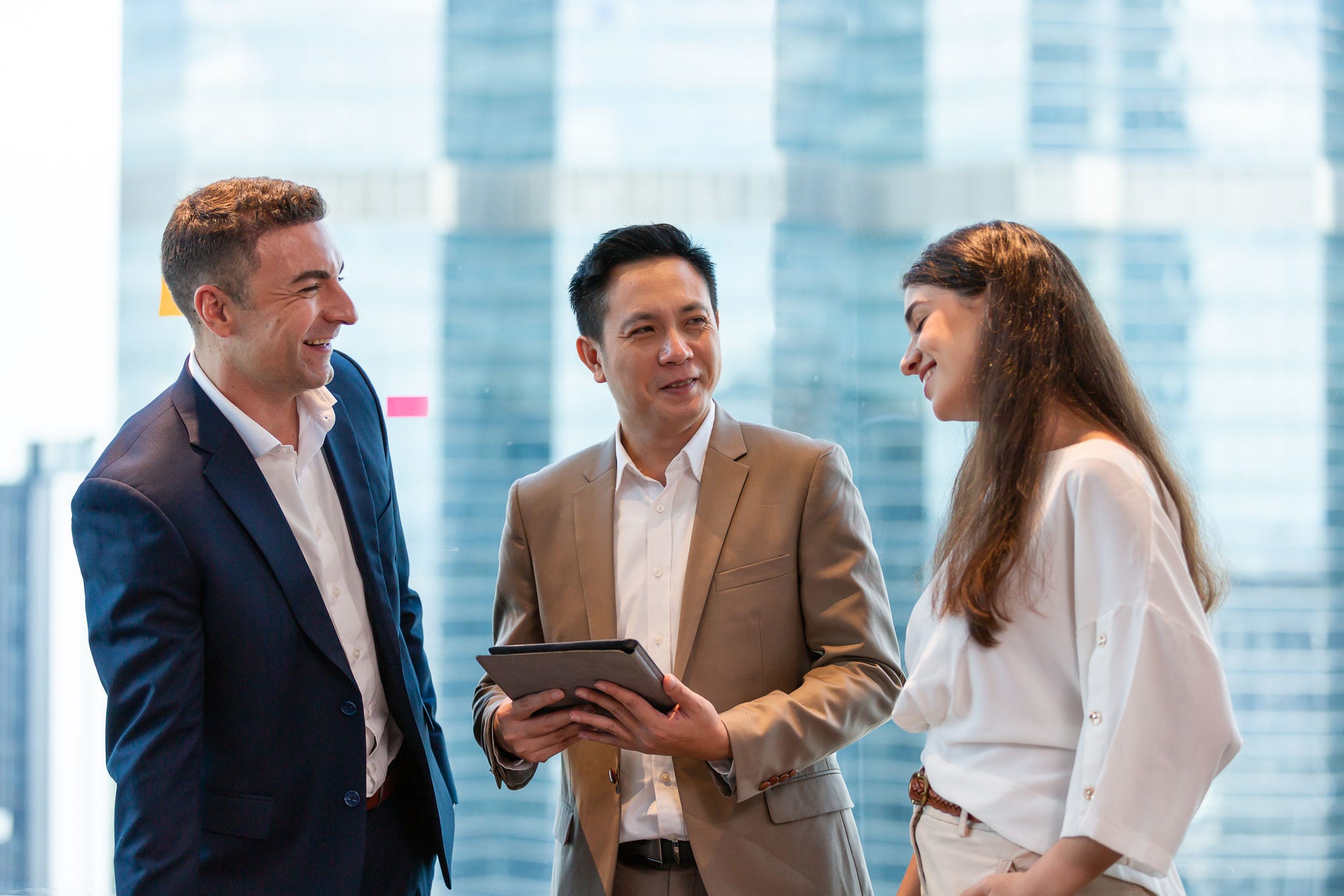 Smiling group of diverse businesspeople discussing in the office with cityscape blur background. Young businessmen and businesswoman talking in meeting room after the meeting. business, people, office