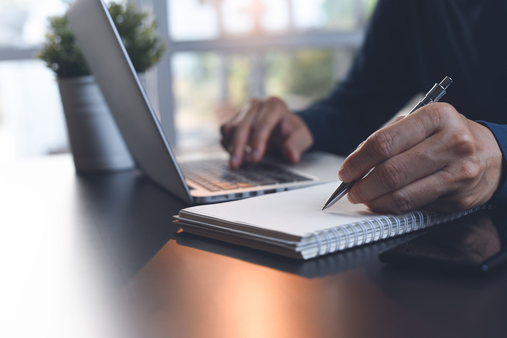 E-learning, online study, learn from home, teleworking concept. Close up, business man hand with pen writing on notebook, working with laptop computer on desk at home office. Student studying online, lecturing on notepad, close up