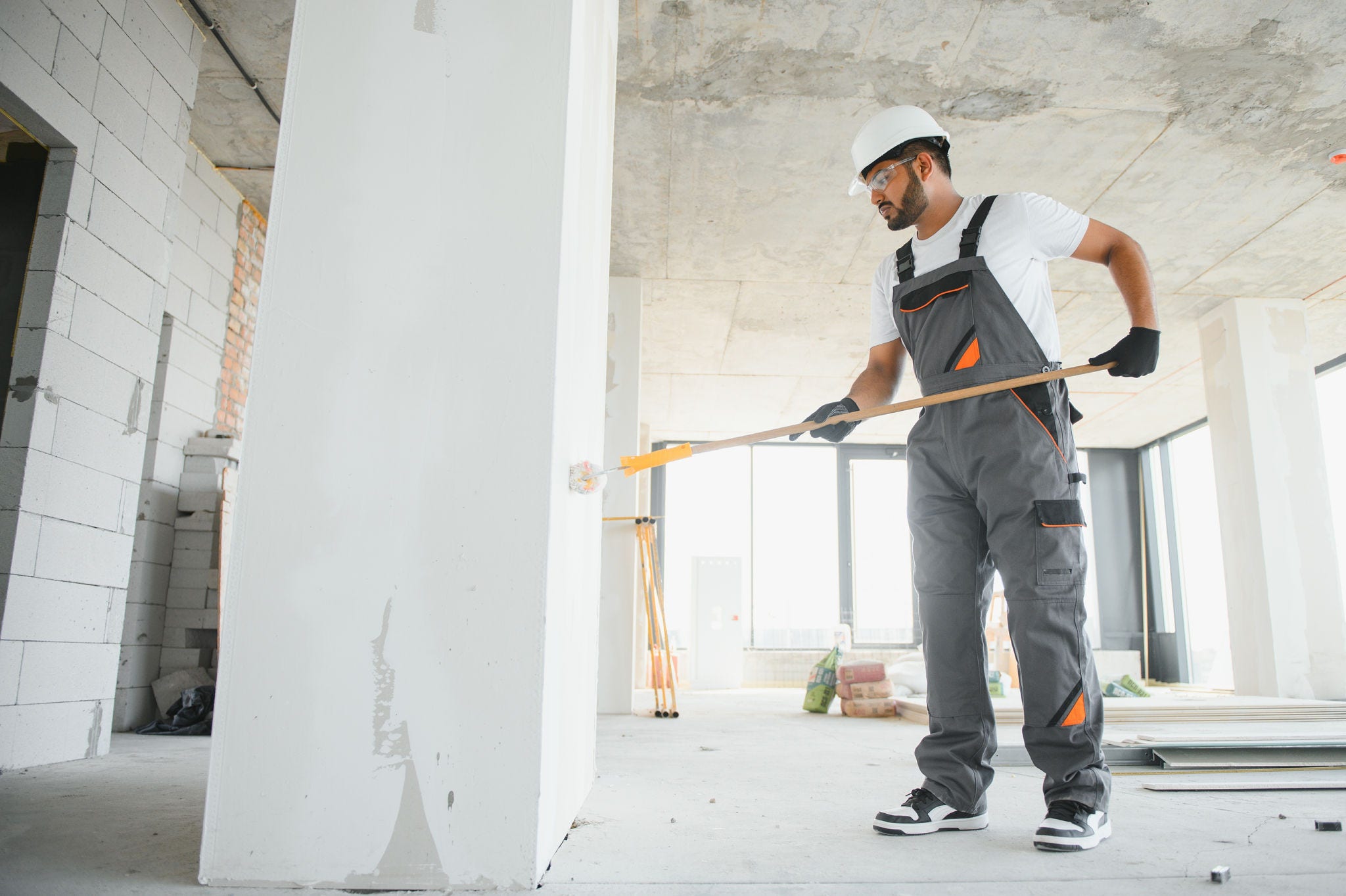 An Indian apartment repair worker paints a white wall with a roller.