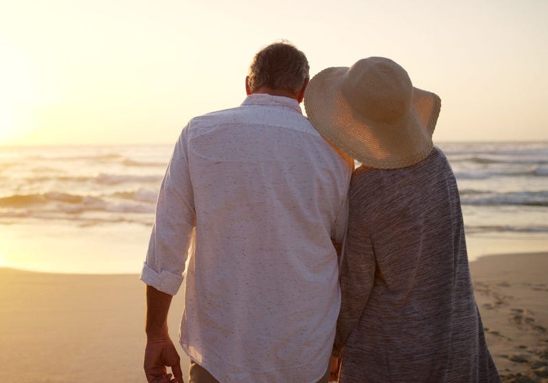 Old couple, beach and sunset with ocean view on vacation, memory and space with back in summer. Elderly people, partner and outdoor with bonding, love or holding for hands on holiday in retirement