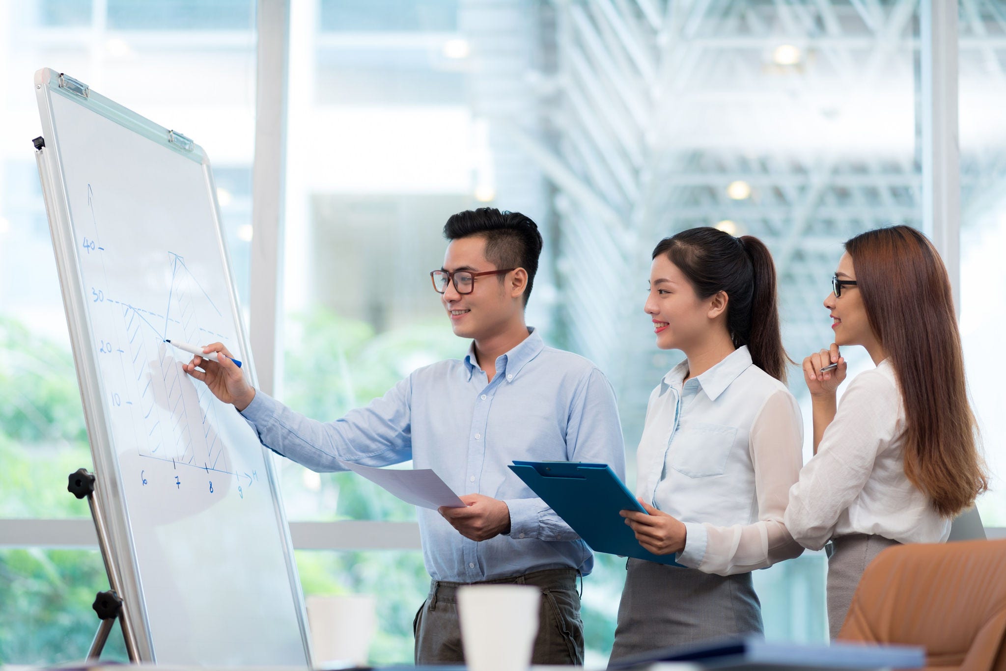 Young Vietnamese businessman explaining chart on the whiteboard to his colleagues