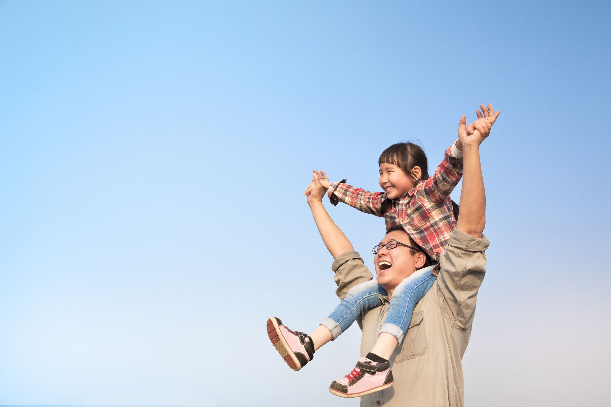 happy Father carrying his daughter on shoulders with blue sky background
