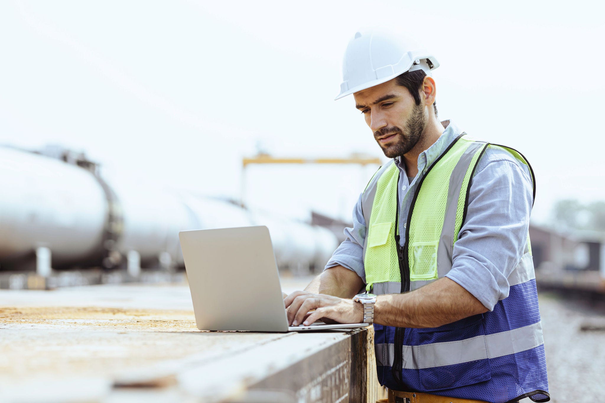 Man at a industrial site looking at a laptop