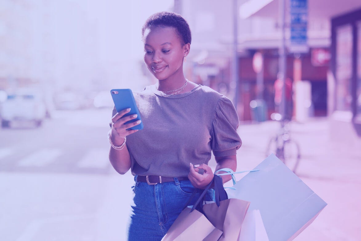 Woman smiling while checking her cell phone with shopping bags in her hand.