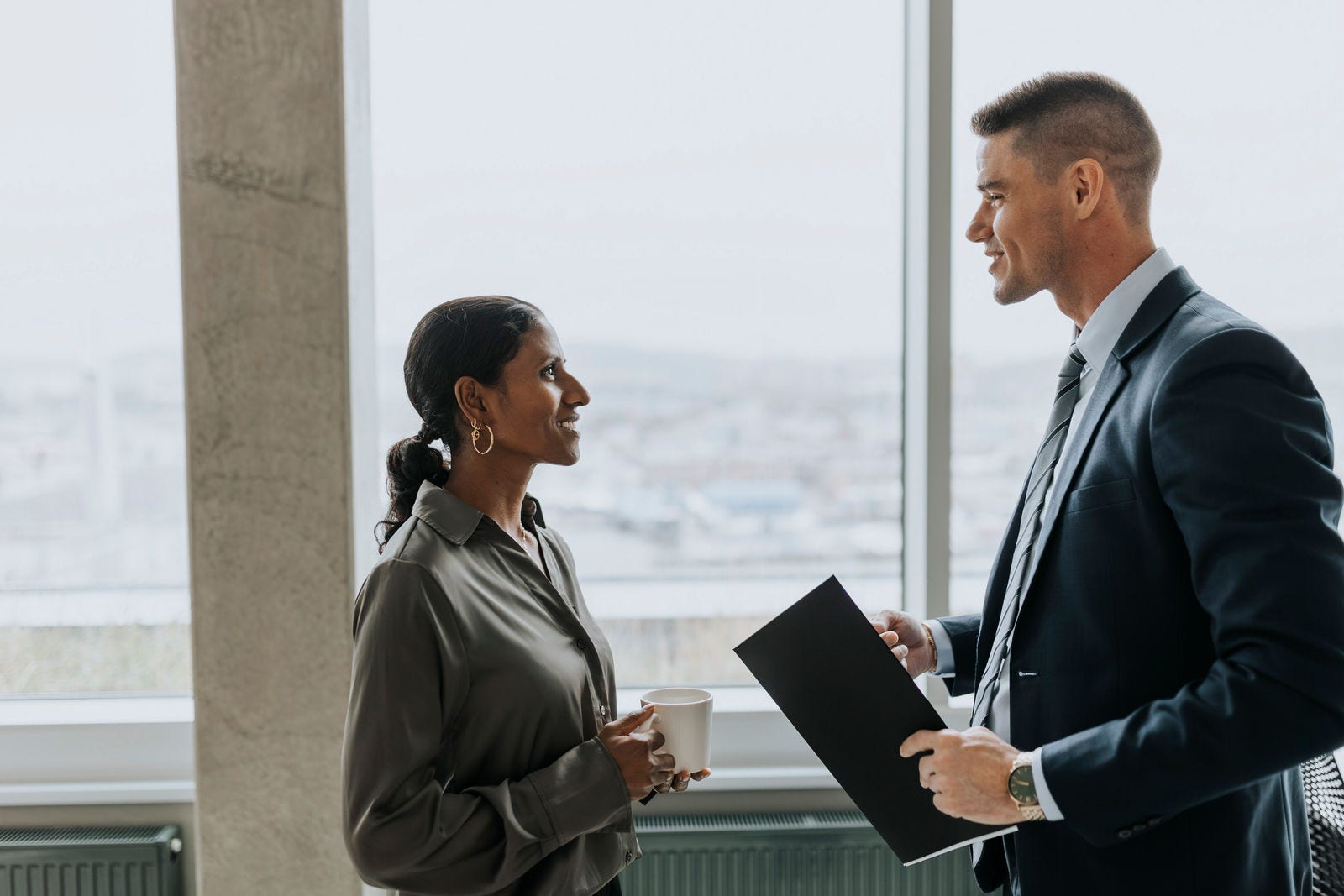 Side view of smiling business colleagues with coffee cup and document standing in office