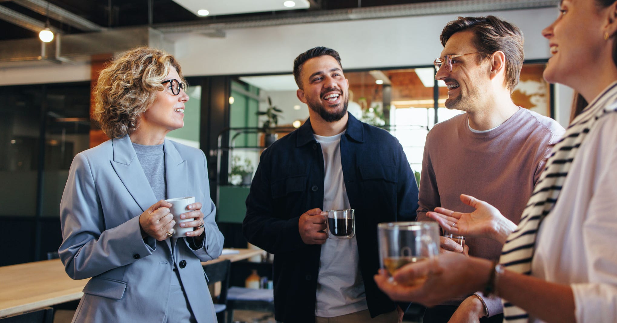 Happy colleagues having a coffee break in an office. Group of business people having a conversation in a workplace. Business professionals working in a startup.