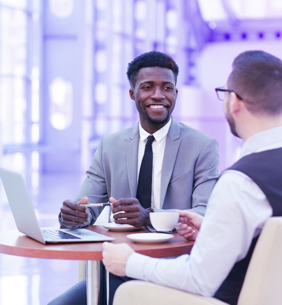 Young man meeting another man for a coffee. On the table in front of them, there's a laptop.