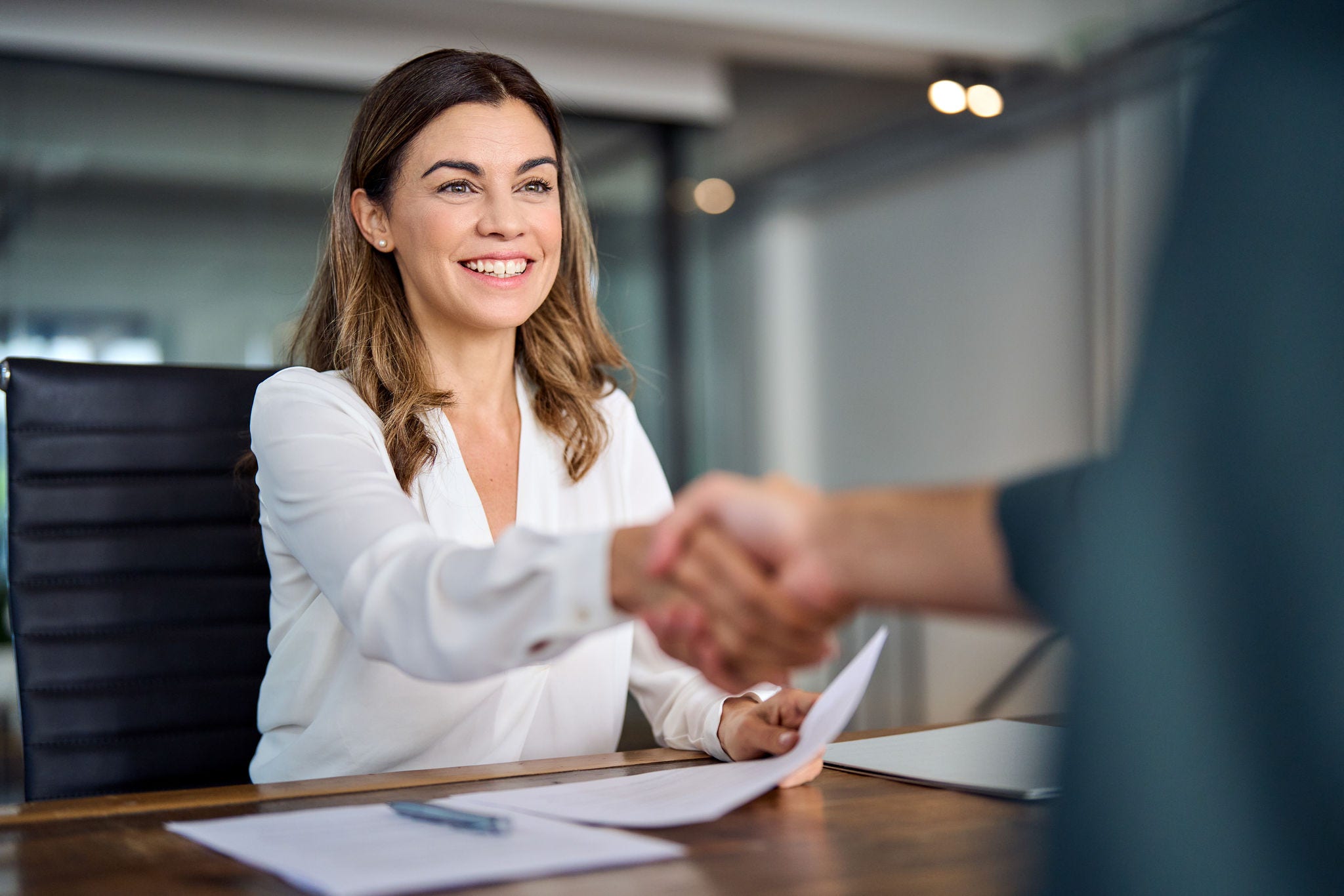 Happy mid aged business woman manager handshaking at office meeting. Smiling female hr hiring recruit at job interview, bank or insurance agent, lawyer making contract deal with client at work.