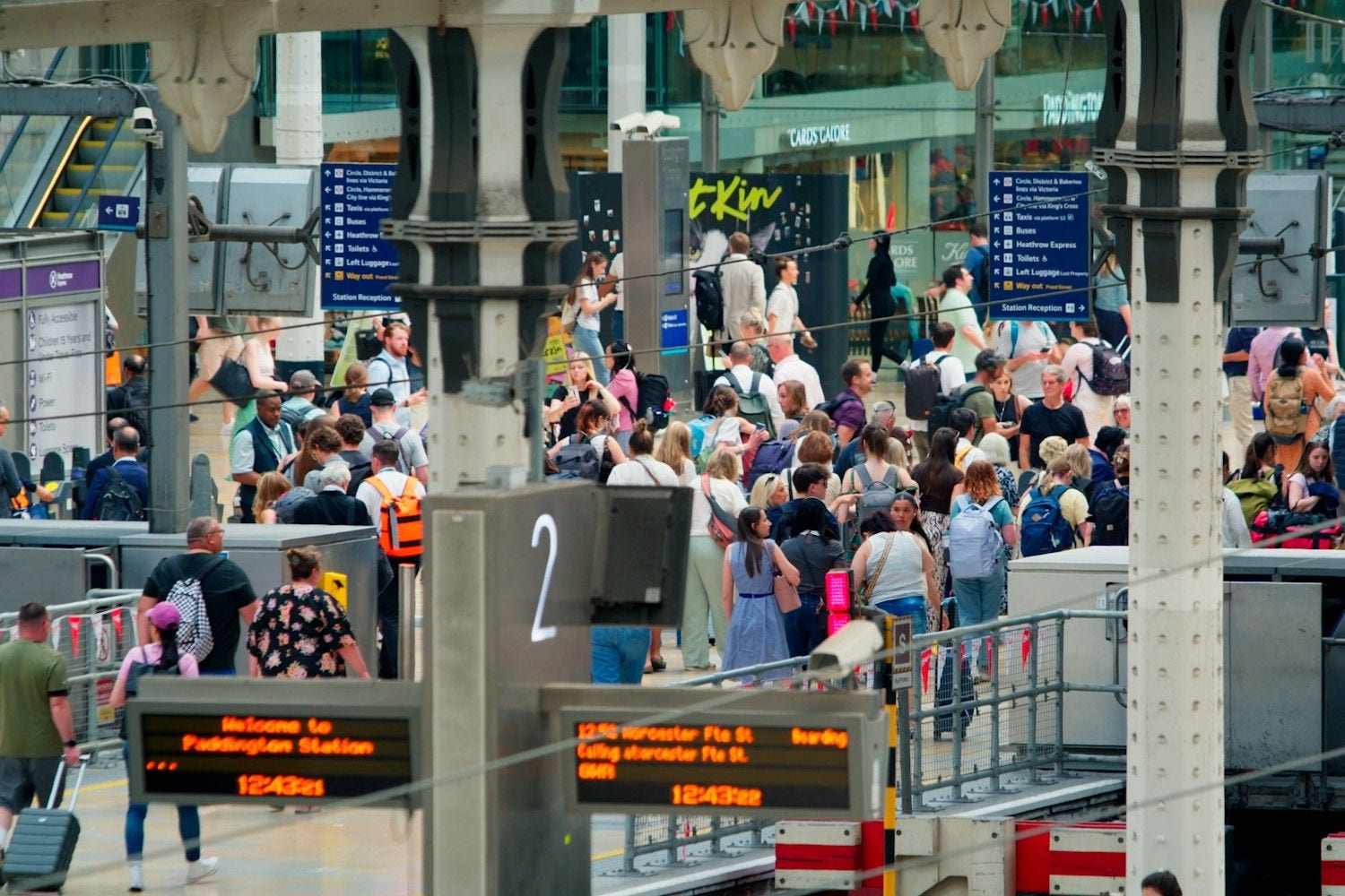 Crowded railway station platform with passengers and wayfinding signage.
