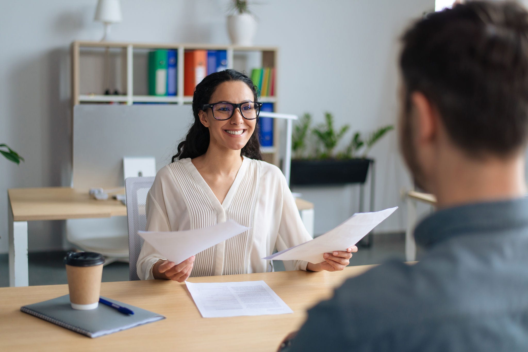 Searching for job concept. Happy human resources manager speaking to employment applicant on work interview, holding CV at office. Personnel manager talking to vacancy candidate