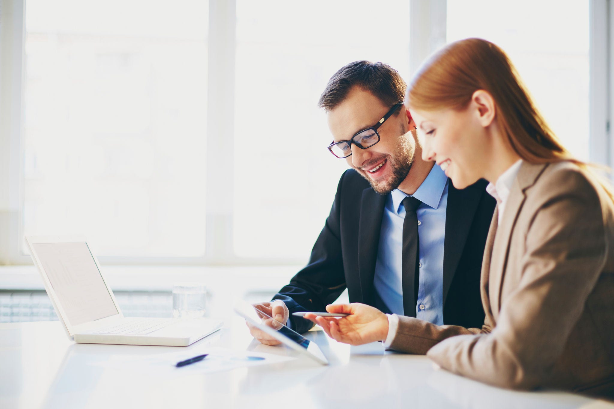 Image of two young business partners using touchpad at meeting