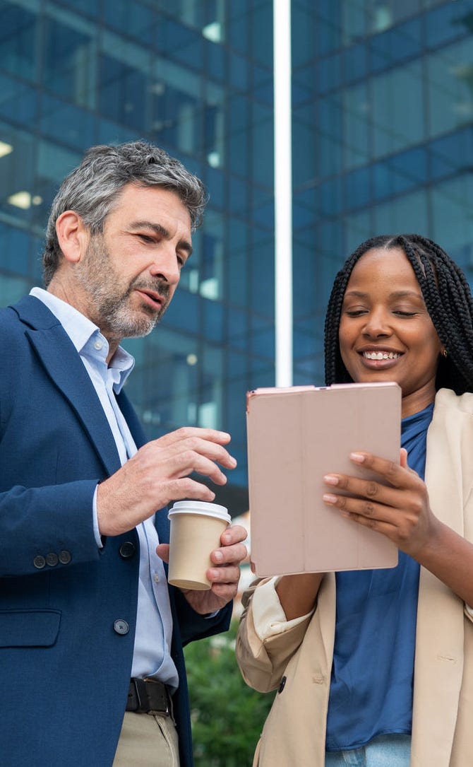 Diverse business people collaborating on a digital tablet in front of a modern office building