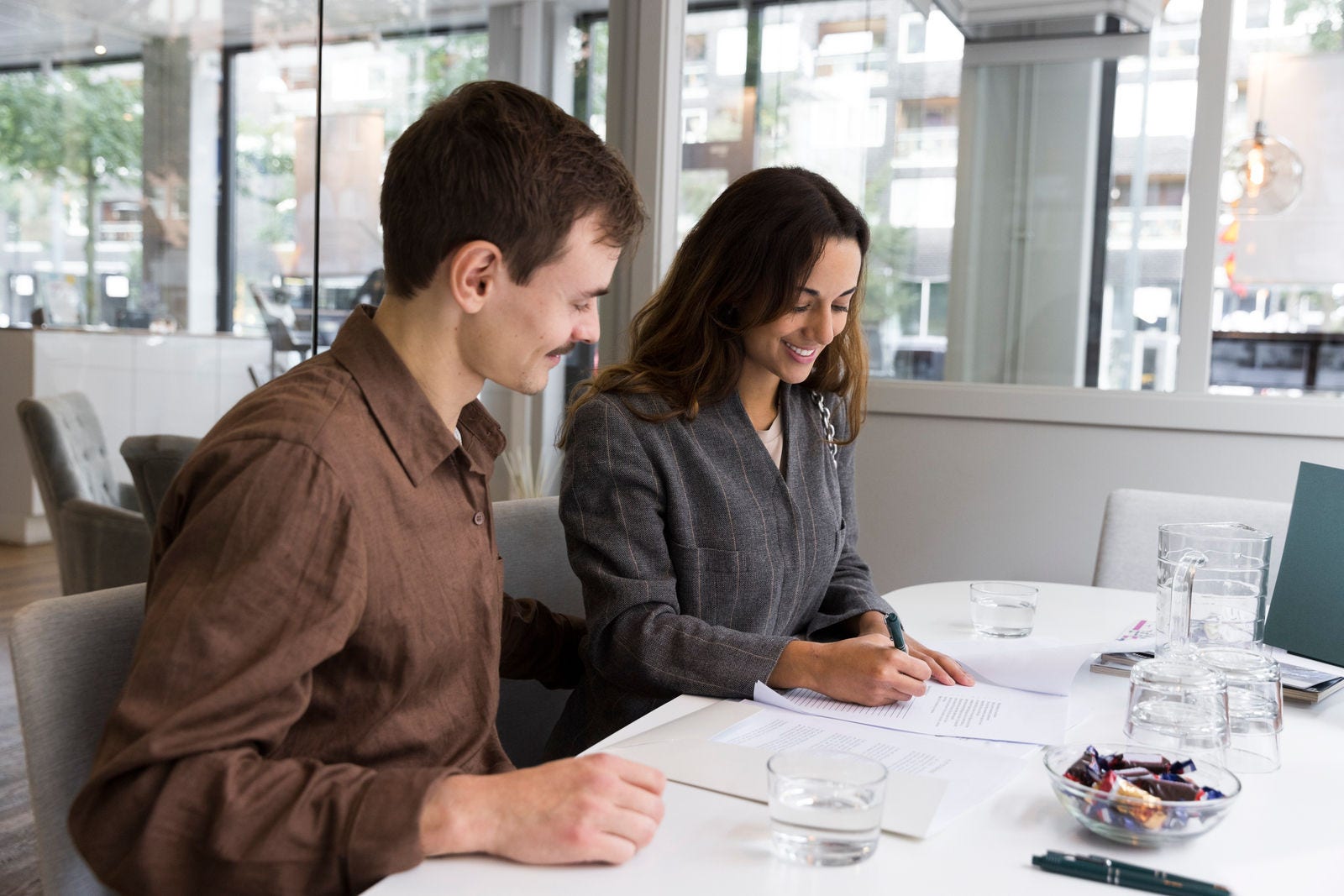 Man looking at woman smiling while signing agreement at desk in real estate office