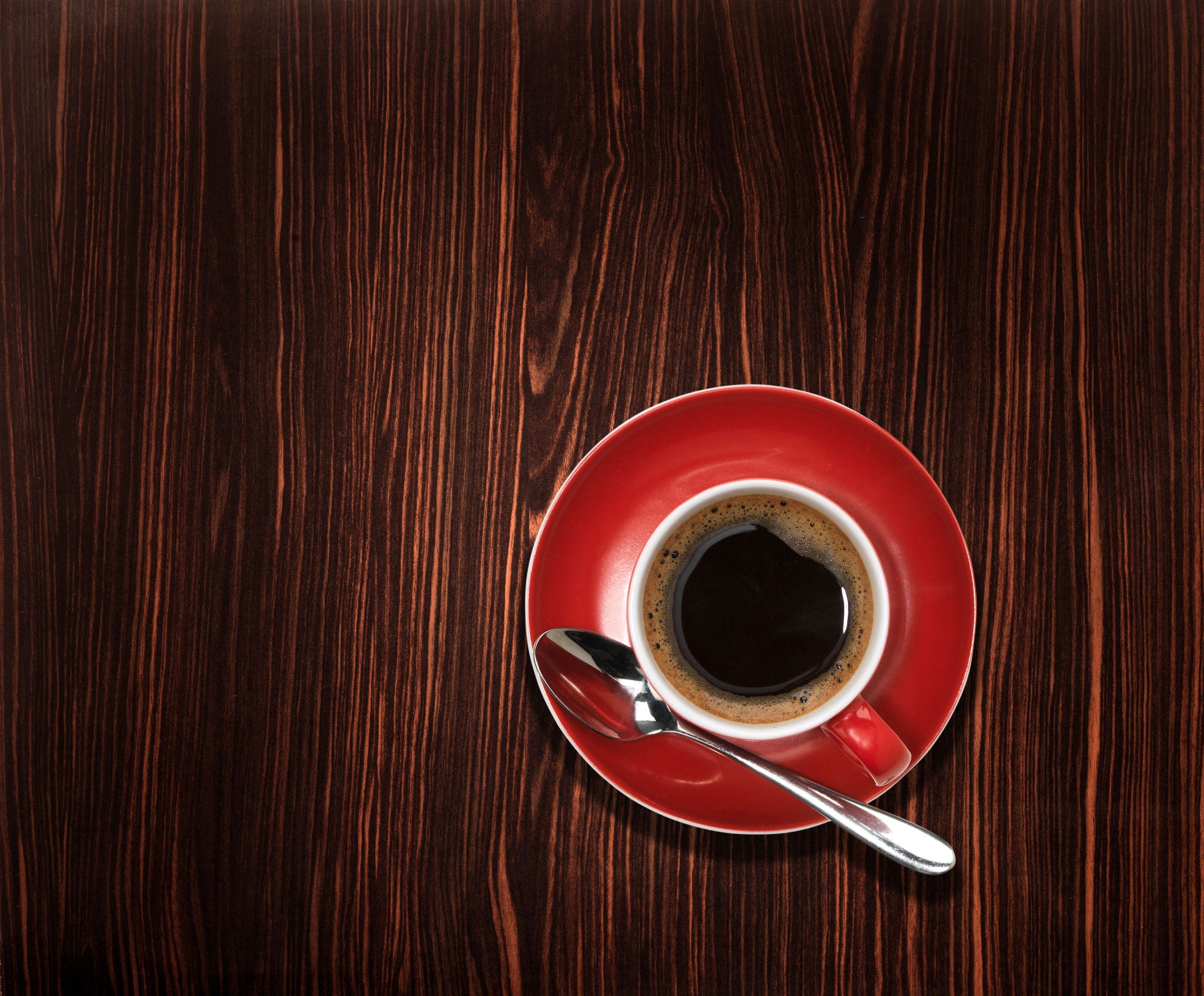 Overhead view of an espresso coffee on wooden table. Keywords: 2015, Caffeine Molecule, Coffee - Drink, Colour Image, Copy Space, Drink, Elevated View, Espresso, Freshness, Horizontal, Indoors, Italian Culture, No People, Photography, Red, Refreshment, Saucer, Single Object, Still Life, Table, Teaspoon, Wood - Material 