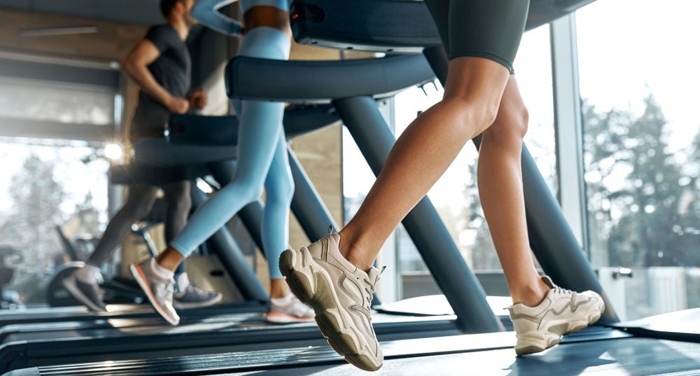 Dynamic low-angle view of three people running indoors on treadmills. Focus on legs in motion, concept of sport and active lifestyle.