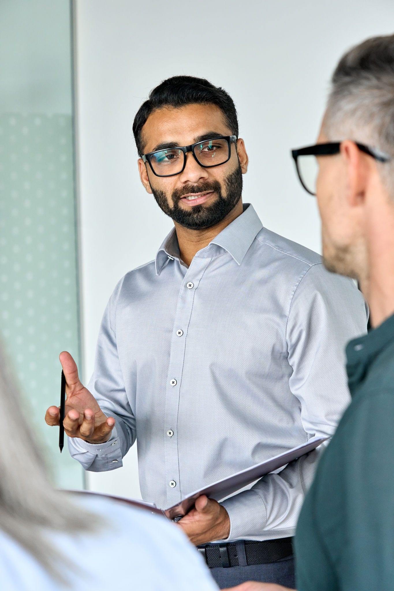Diverse executive business team group listening to Indian executive ceo holding contract discussing project standing at boardroom meeting. Multiracial team doing paperwork in office. Vertical.