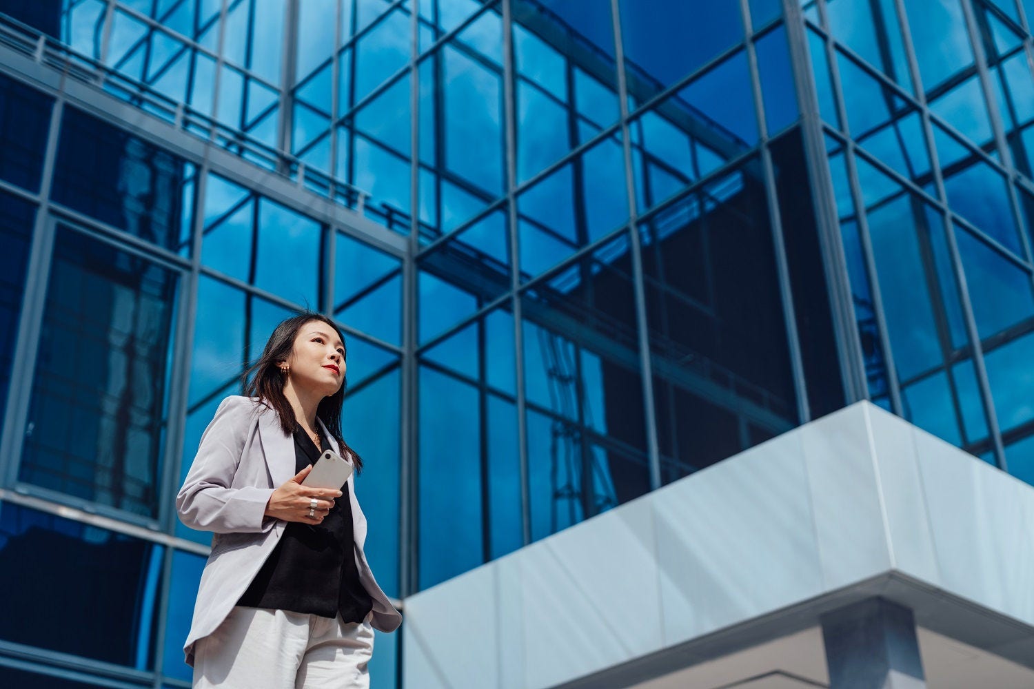 Low angle view of young Asian woman walking against commercial building. Female leadership in workplace. Young entrepreneur.
