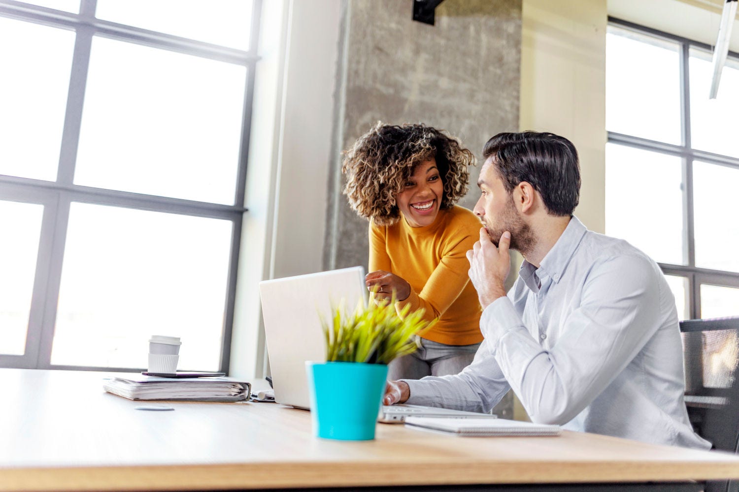 Business project team working together at meeting room at office. Smiling work colleagues sitting together at a table in a modern office talking and using a laptop.