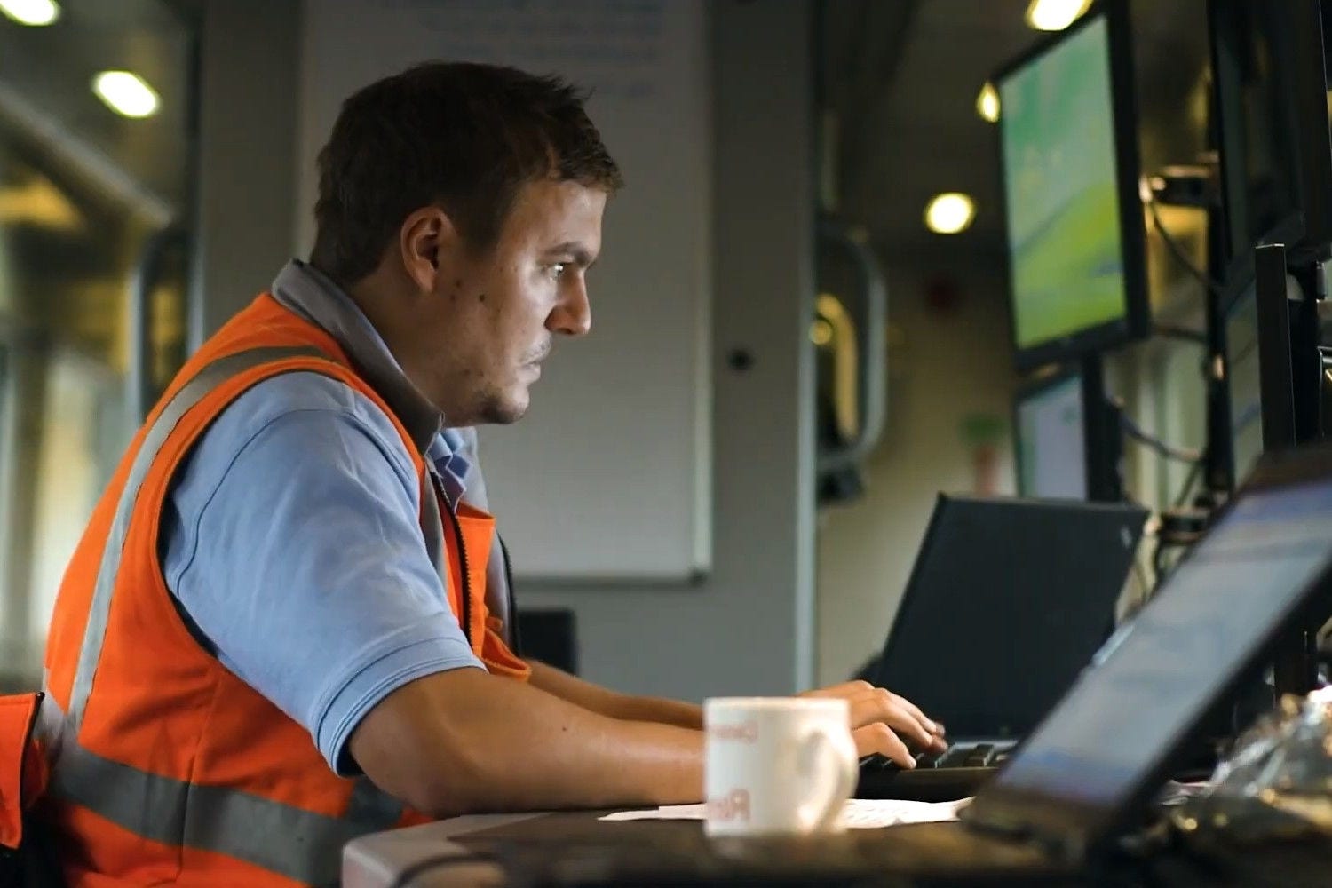 Rail worker monitoring railway operations using multiple computer screens.