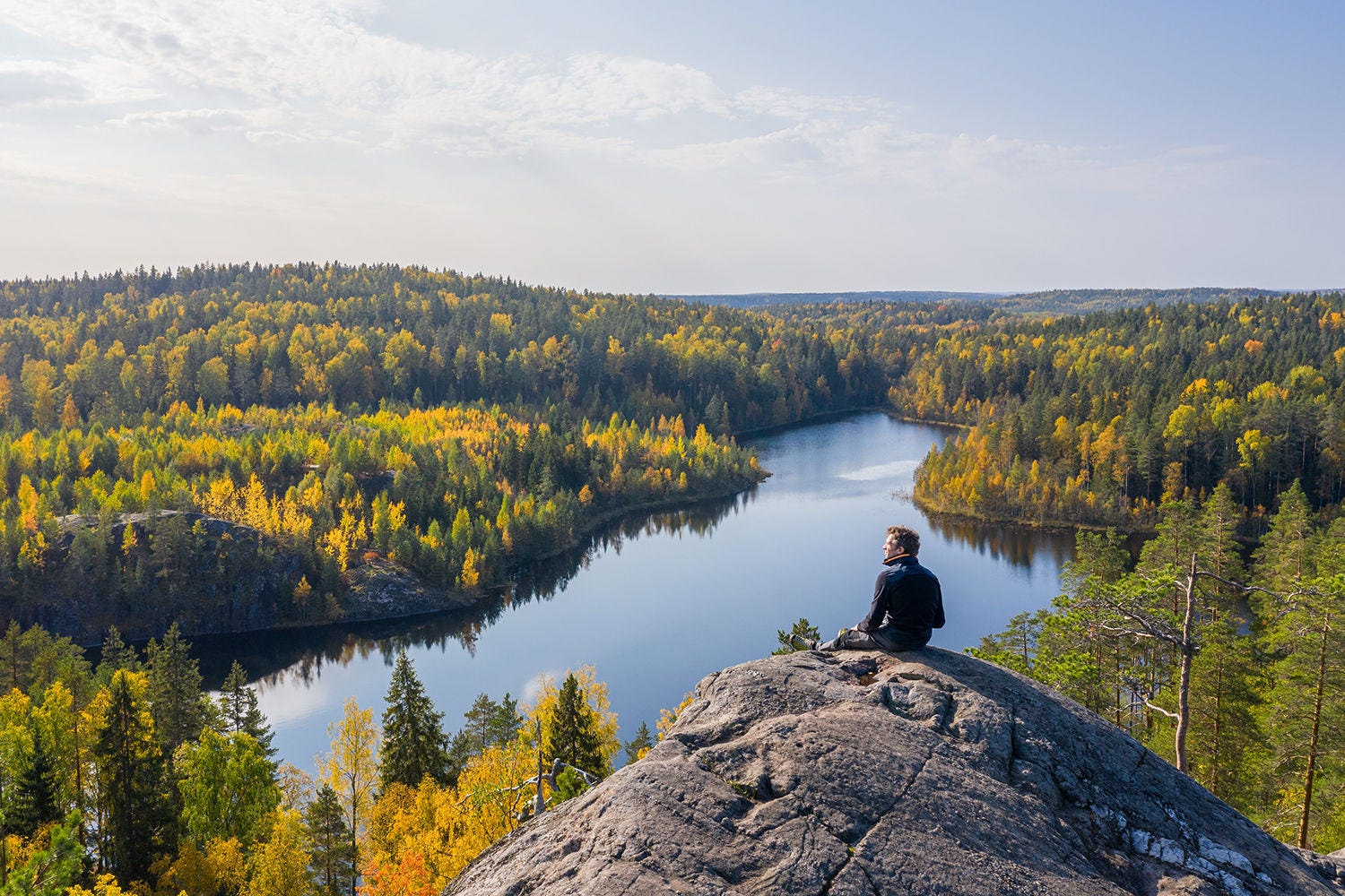 男人站在秋天森林里的一块岩石上，背景是一个美丽的湖泊