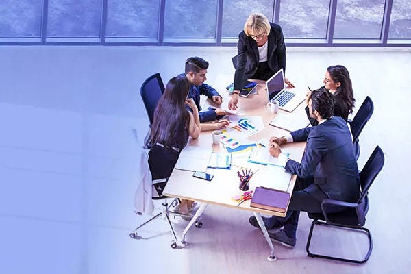 Cinco pessoas discutindo ideias e vendo gráficos de dados numa mesa grande de escritório