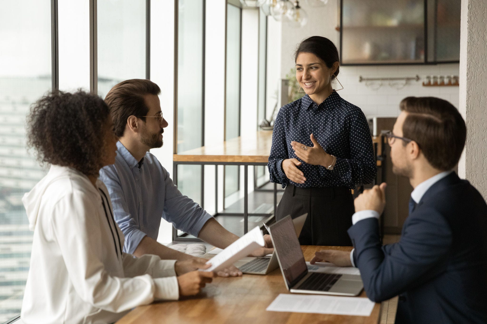 Smiling Indian businesswoman leading corporate meeting with diverse colleagues, coach mentor training employees, discussing project strategy, sharing ideas, business partners negotiation concept