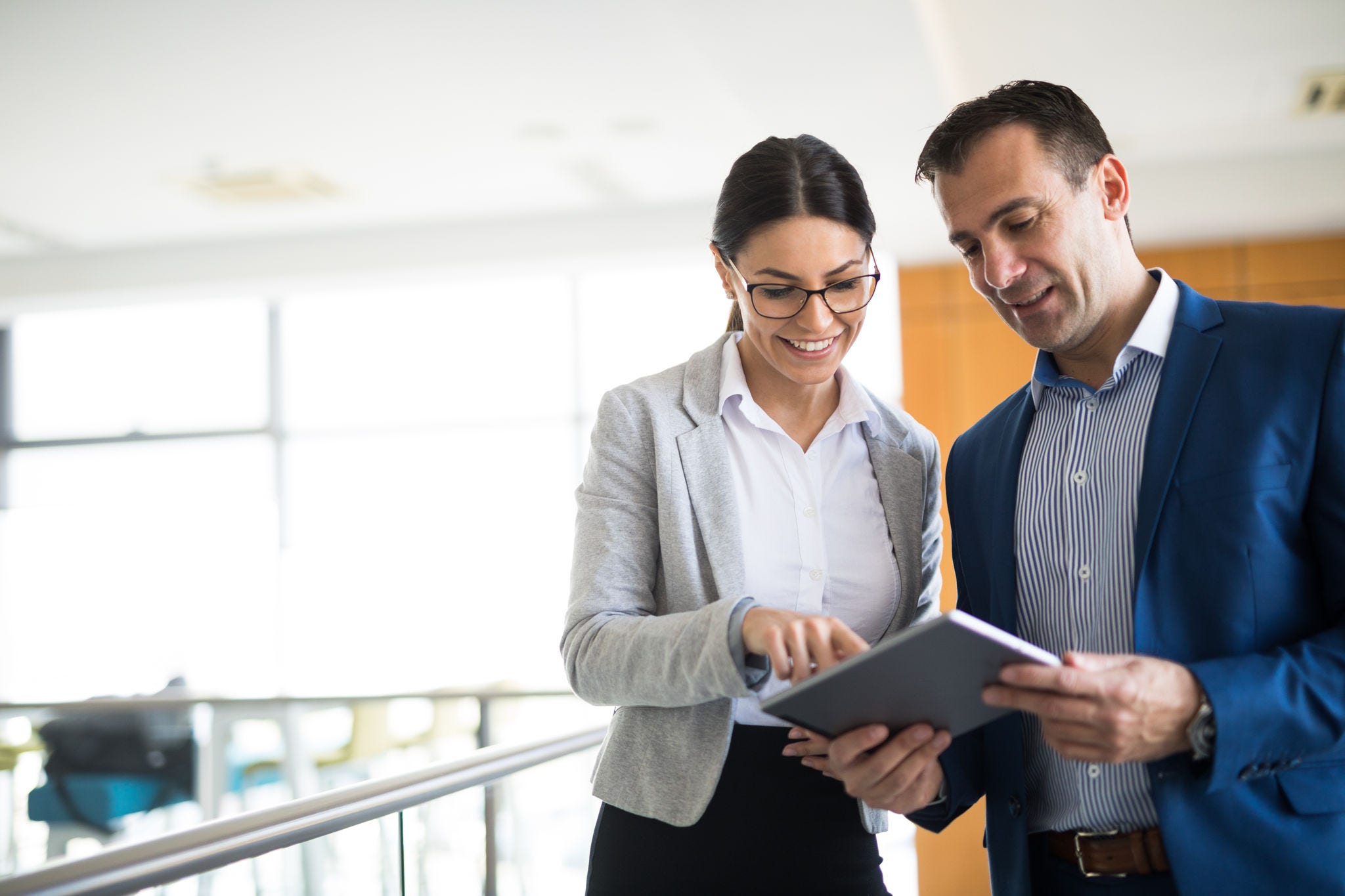 Two mixed-age business people are discussing business strategy in the office building hallway using digital tablet. Front view. Copy space.